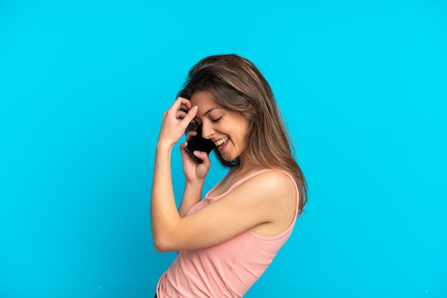 Young caucasian woman using mobile phone isolated on blue background laughing