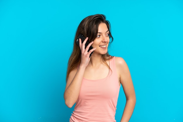 Young caucasian woman using mobile phone isolated on blue background looking side