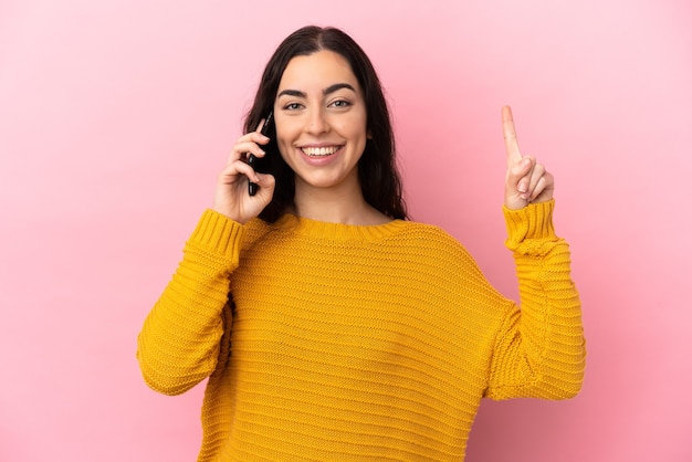 Young caucasian woman using mobile phone isolated on pink background pointing up a great idea