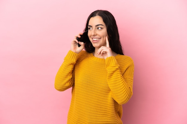 Giovane donna caucasica che utilizza il telefono cellulare isolato su sfondo rosa pensando a un'idea mentre guarda in alto