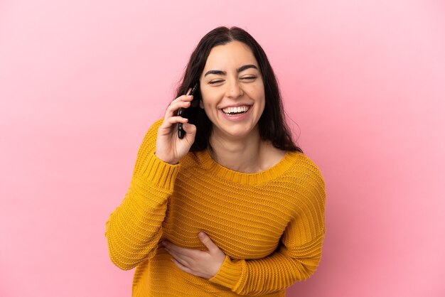 Young caucasian woman using mobile phone isolated on pink wall smiling a lot