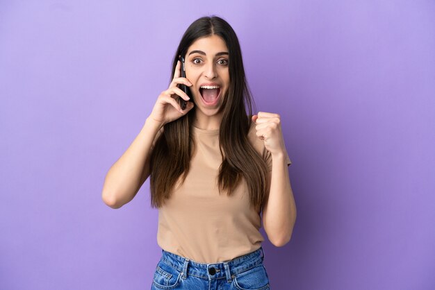 Young caucasian woman using mobile phone isolated on purple background celebrating a victory in winner position