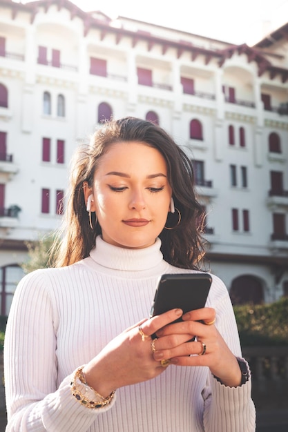 Giovane donna caucasica che utilizza uno smartphone davanti a un edificio bianco