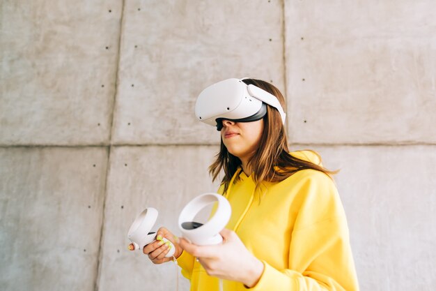 VRヘッドセットを使用し、コントローラーを保持し、仮想現実を見ている若い白人女性。