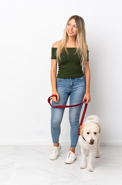 Young caucasian woman walking the dog isolated on white background looking to the side and smiling