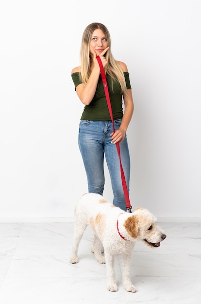 Young caucasian woman walking the dog on white having doubts