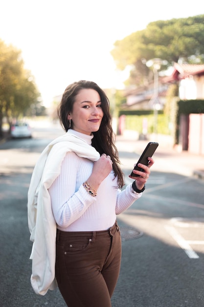 Giovane donna caucasica che cammina per strada utilizzando uno smartphone