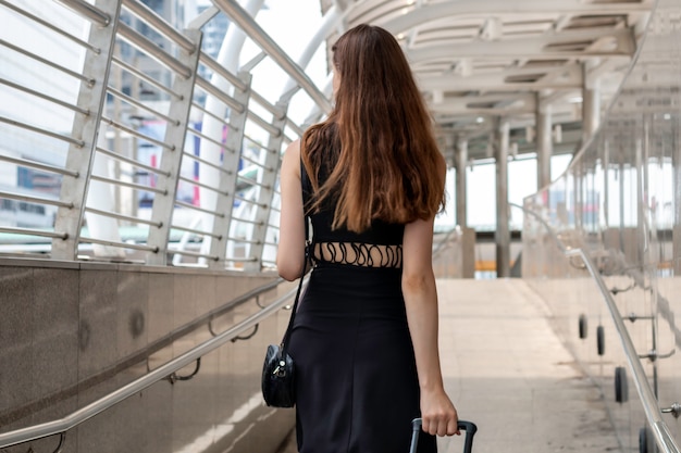 現代の空港ターミナルでスーツケースを持って歩く若い白人女性。幸せな旅行者の背面図。