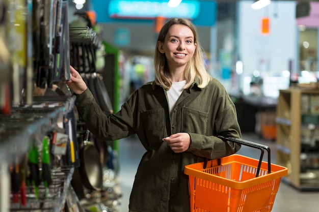 Young caucasian woman walks between rows of supermarket with a basket in hands. Female Shopping Through Goods Section, Browsing. Big Store with Lots of Aisles. in grocery store chooses goods examining