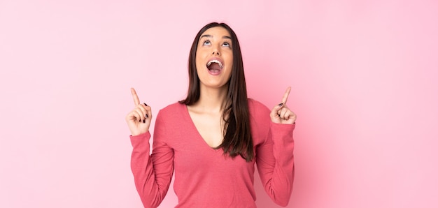 Young caucasian woman over wall surprised and pointing up