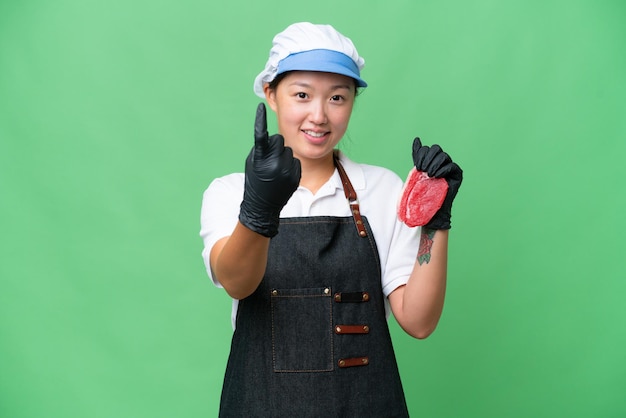 Young caucasian woman wearing an apron and serving fresh cut meat over isolated background doing coming gesture