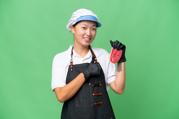 Young caucasian woman wearing an apron and serving fresh cut meat over isolated background giving a thumbs up gesture