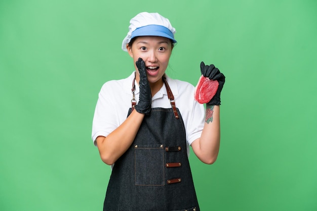 Young caucasian woman wearing an apron and serving fresh cut meat over isolated background with surprise and shocked facial expression