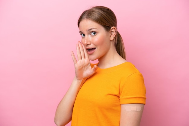 Young caucasian woman wearing band aid isolated on pink background whispering something