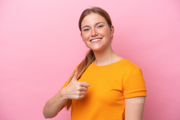 Young caucasian woman wearing band aid isolated on pink background with thumbs up because something good has happened