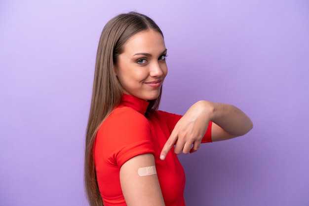 Young caucasian woman wearing band aid isolated on purple background and pointing it