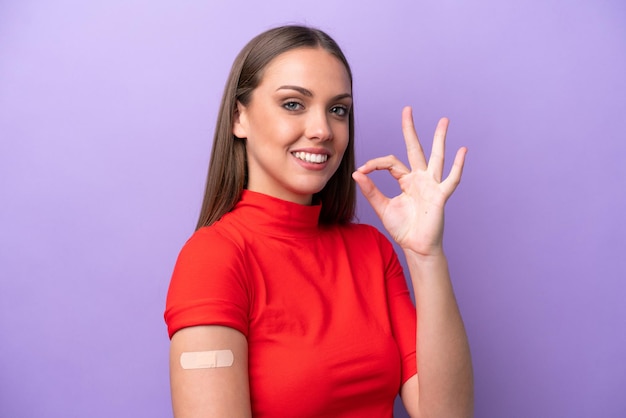 Young caucasian woman wearing band aid isolated on purple background showing ok sign with fingers