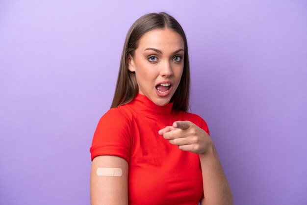 Young caucasian woman wearing band aid isolated on purple background surprised and pointing front