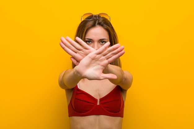 Young caucasian woman wearing bikini and sunglasses doing a denial gesture