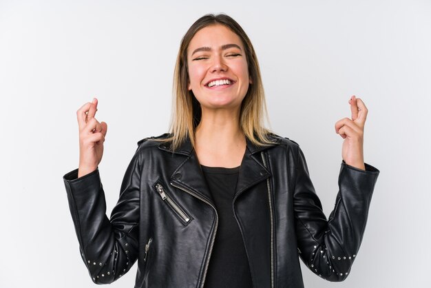 Young caucasian woman wearing a black leather jacket crossing fingers for having luck