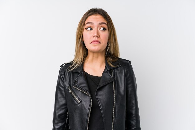 Young caucasian woman wearing a black leather jacket shrugs shoulders and open eyes confused.