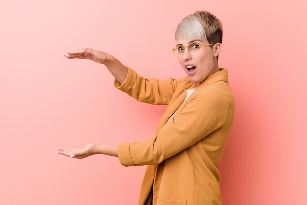 Young caucasian woman wearing a casual business clothes shocked and amazed holding a copyspace between hands.