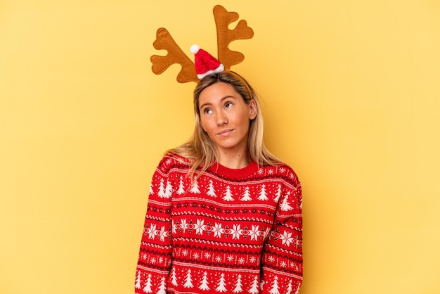 Young caucasian woman wearing a christmas reindeer hat isolated on beige background dreaming of achieving goals and purposes