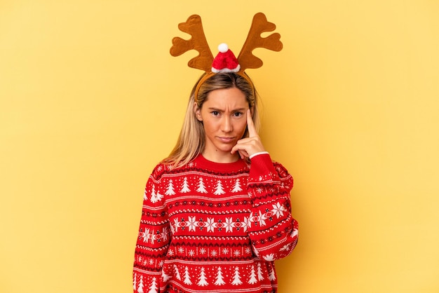Young caucasian woman wearing a christmas reindeer hat isolated on beige background pointing temple with finger, thinking, focused on a task.