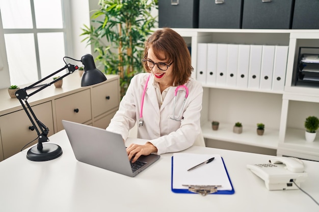 Young caucasian woman wearing doctor uniform using laptop at clinic