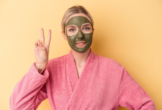 Young caucasian woman wearing face mask isolated on yellow background showing number two with fingers.