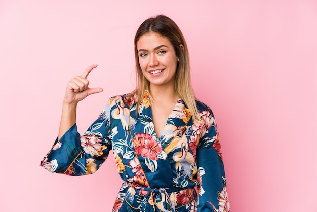 Young caucasian woman wearing pajamas holding something little with forefingers, smiling and confident.