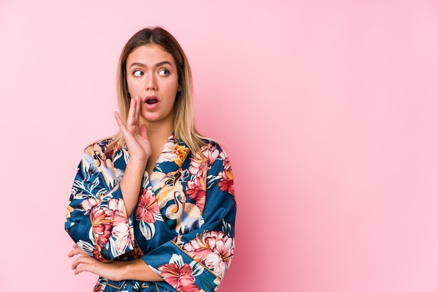 Young caucasian woman wearing pajamas is saying a secret and looking aside