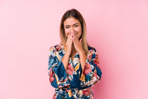 Young caucasian woman wearing pajamas laughing about something, covering mouth with hands.