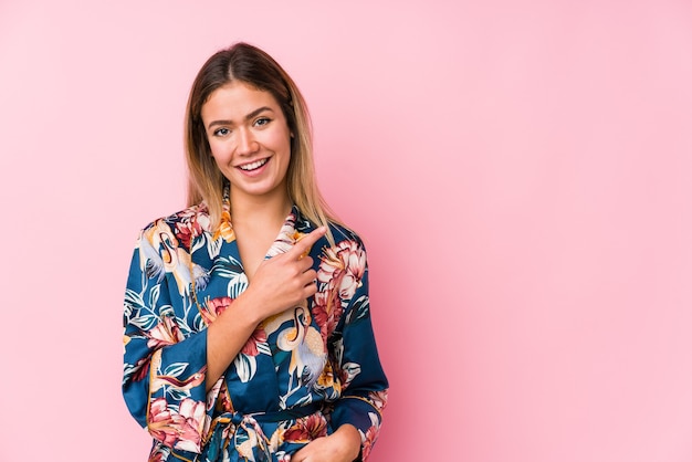 Young caucasian woman wearing pajamas smiling and pointing aside, showing something at blank space.