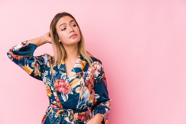 Young caucasian woman wearing pajamas touching back of head, thinking and making a choice.