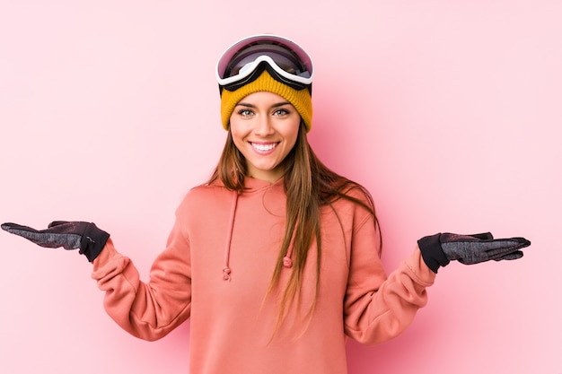 Young caucasian woman wearing a ski clothes isolated makes scale with arms, feels happy and confident.