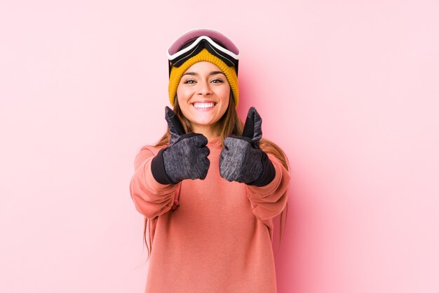 親指アップで分離されたスキー服を着ている若い白人女性、何かについての歓声、サポートと尊敬の概念。