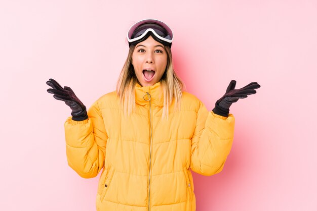 Young caucasian woman wearing a ski clothes in a pink wall celebrating a victory or success, he is surprised and shocked.