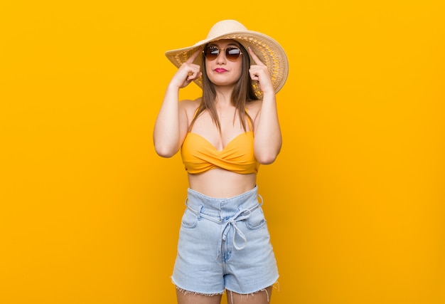 Young caucasian woman wearing a straw hat, summer look focused on a task, keeping forefingers pointing head.