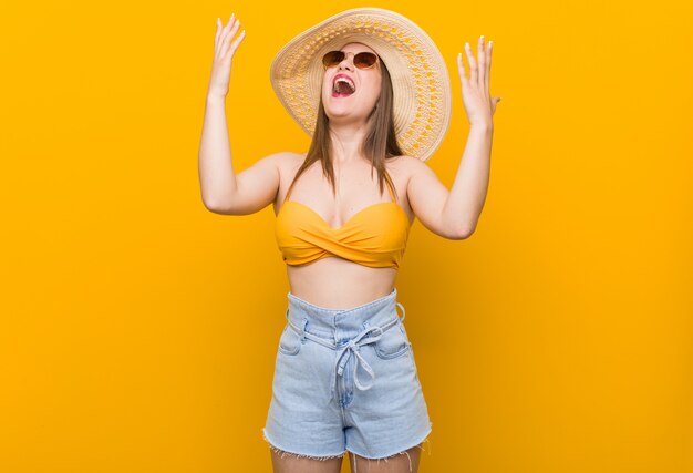 Young caucasian woman wearing a straw hat, summer look screaming to the sky, looking up, frustrated.