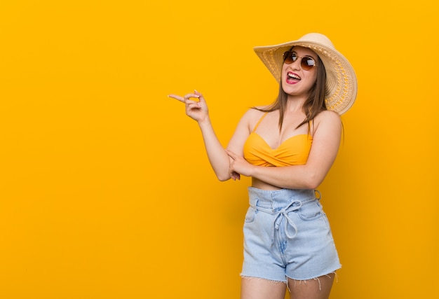 麦わら帽子を身に着けている若い白人女性、人差し指で離れて元気に指している笑みを浮かべて夏の表情。