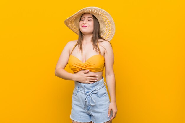 Young caucasian woman wearing a straw hat, summer look touches tummy, smiles gently, eating and satisfaction concept.