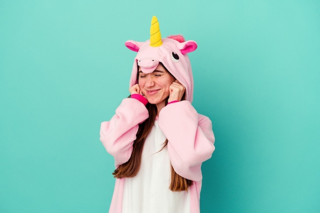 Young caucasian woman wearing a unicorn pajama covering ears with hands.