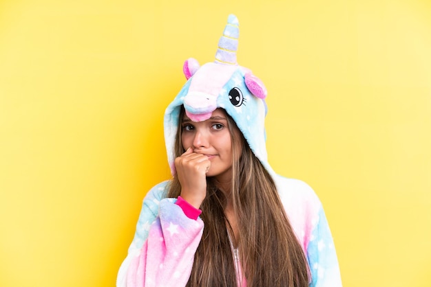 Young caucasian woman wearing a unicorn pajama isolated on yellow background having doubts