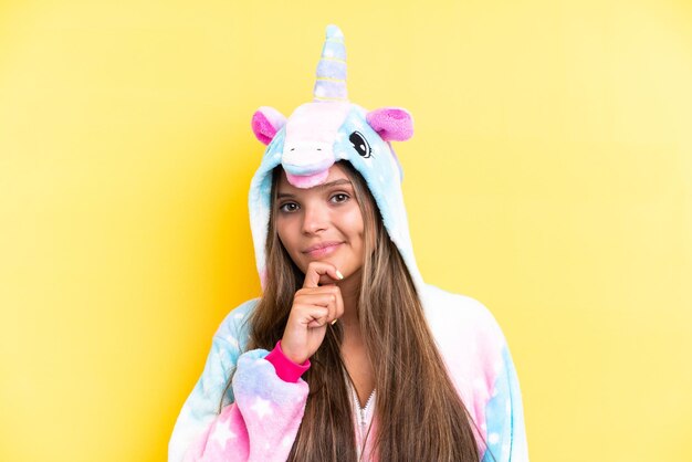 Young caucasian woman wearing a unicorn pajama isolated on yellow background and looking up