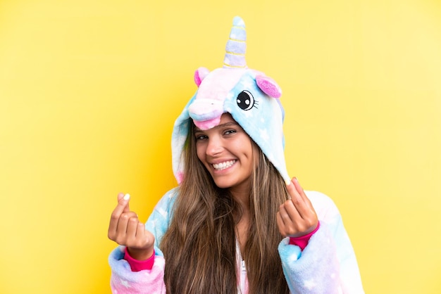 Photo young caucasian woman wearing a unicorn pajama isolated on yellow background making money gesture