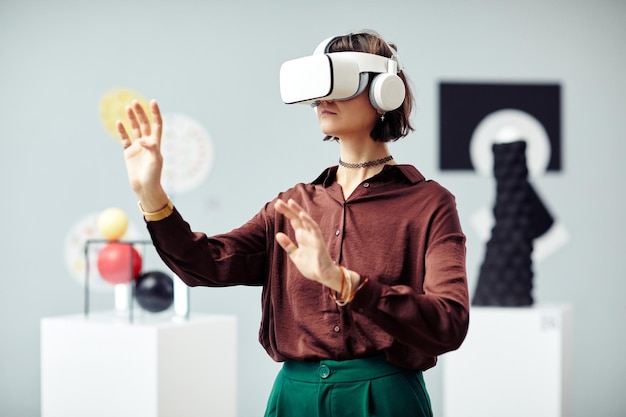 Young caucasian woman wearing vr headset looking at art objects\
while visiting modern exhibition using augmented reality\
technology