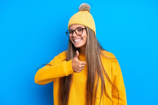 Young caucasian woman wearing winter clothes isolated on blue background giving a thumbs up gesture