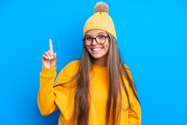 Young caucasian woman wearing winter clothes isolated on blue background pointing up a great idea