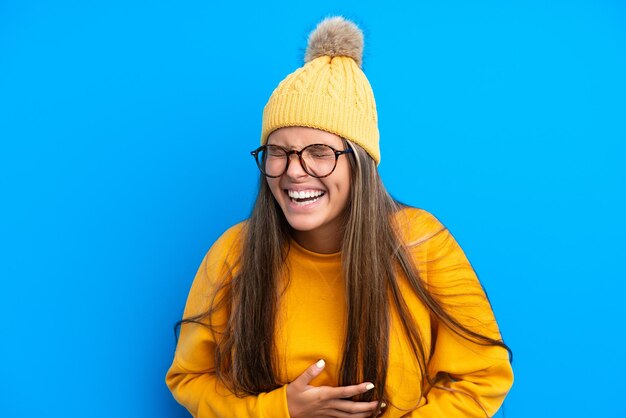 Giovane donna caucasica che indossa abiti invernali isolati su sfondo blu sorridendo molto